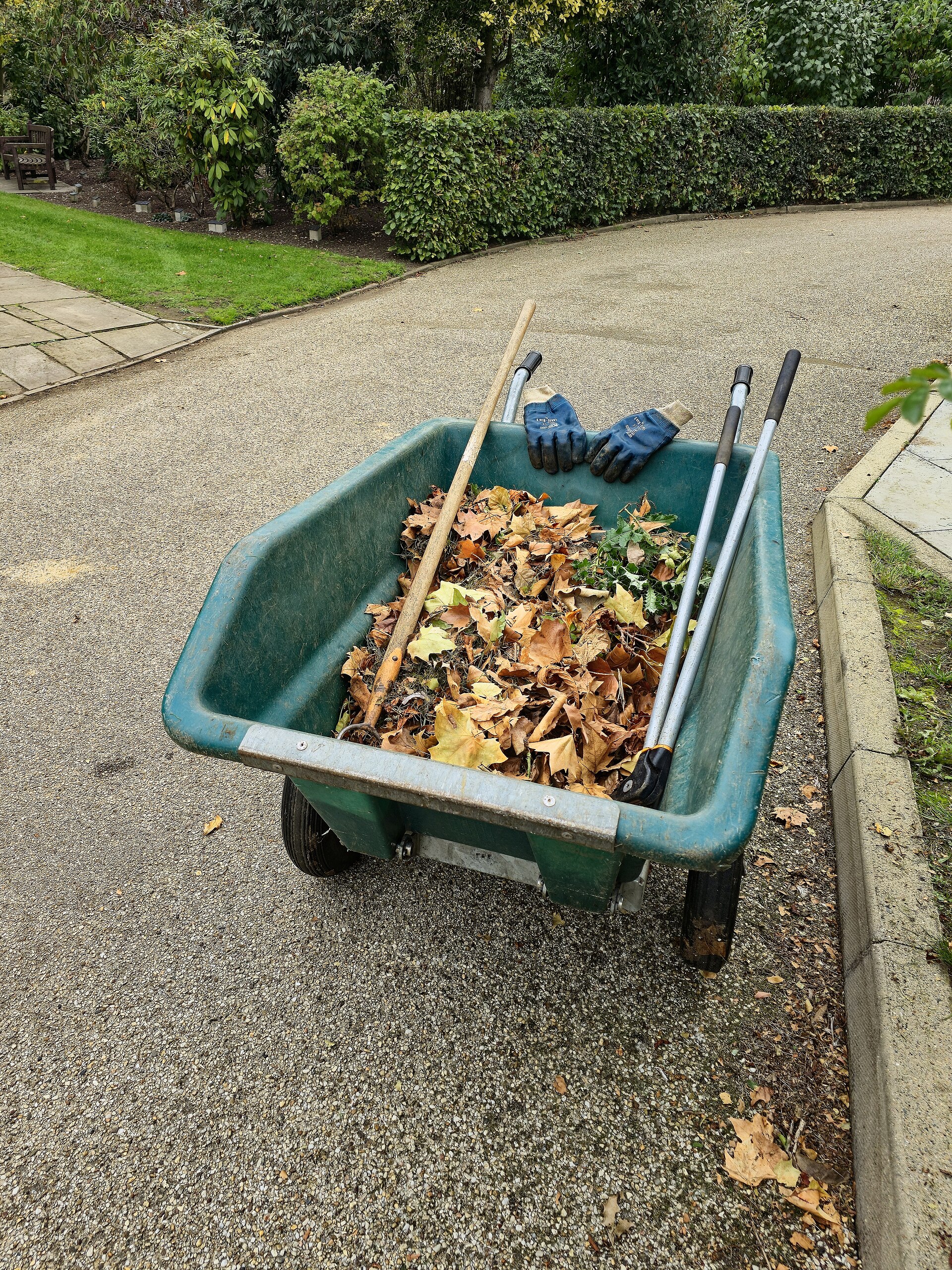 Een kruiwagen vol herfstbladeren met tuinhandschoenen en gereedschap erin