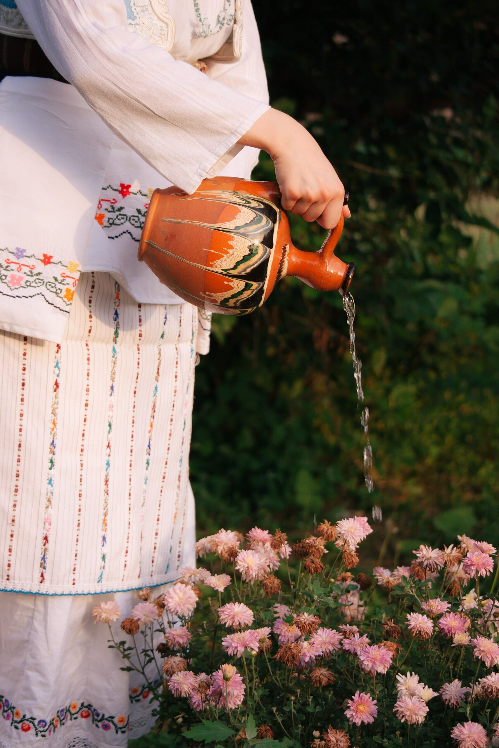 Iemand giet water uit een kan over bloeiende planten in de tuin